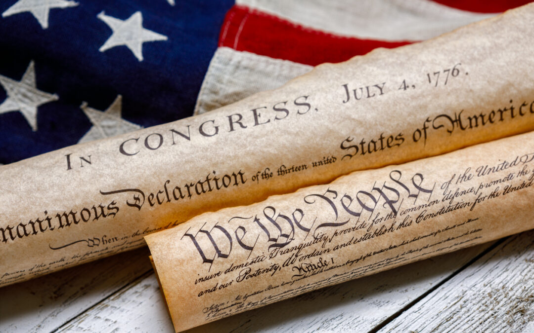 Rolled up copies of the US Constitution and Declaration of Independence with a vintage American flag on white painted weathered wood